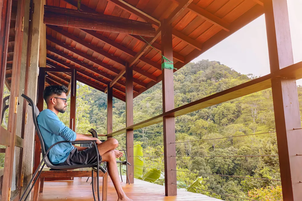 Hombre descansando en el corredor de una casa de madera con vista al bosque
